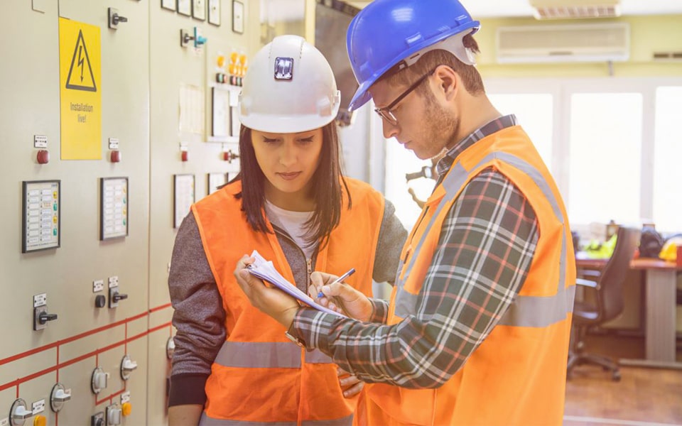 Dos personas con equipo de seguridad examinándola construcción de sistemas eléctricos