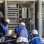 Tres trabajadores con cascos en un panel eléctrico grande, Facility Management Eléctrico