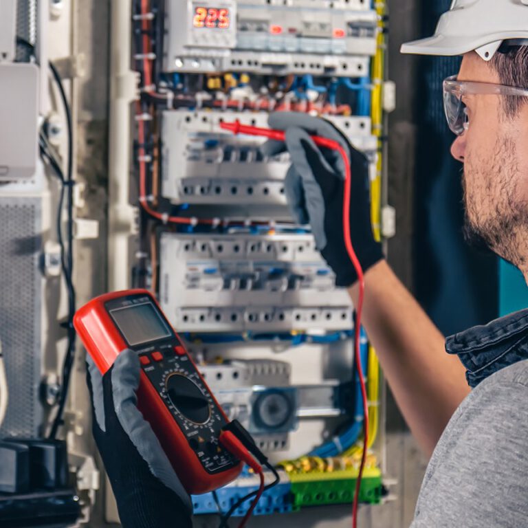 Un hombre sosteniendo un multímetro frente a un panel eléctrico