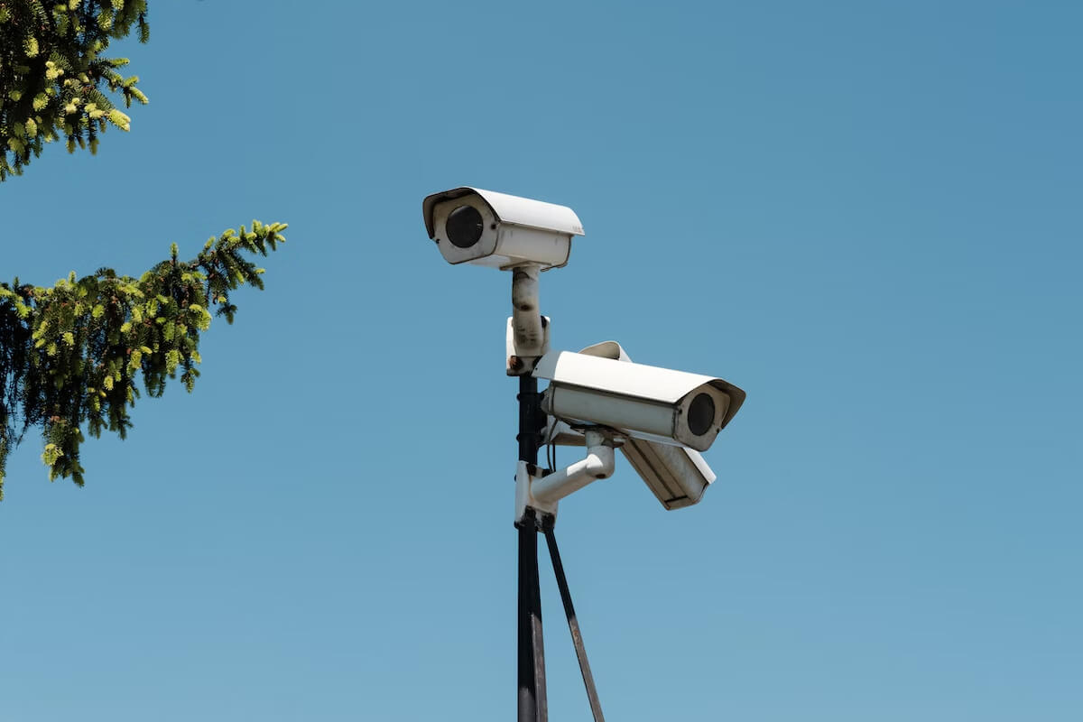 Dos cámaras de seguridad en un poste con un cielo azul de fondo.