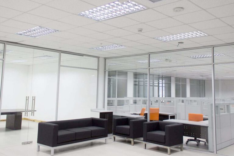 Una oficina con paredes de vidrio, sillas, diseno e iluminacion personalizada.