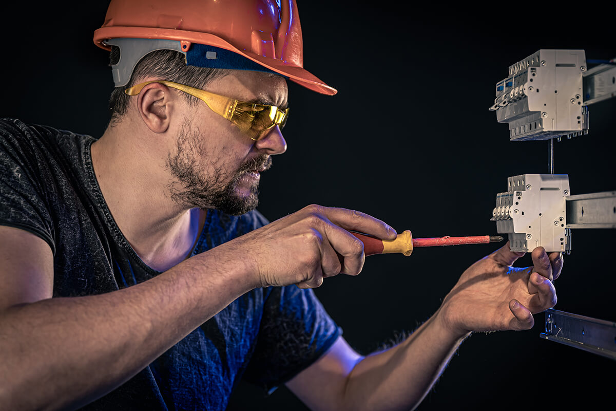 Un hombre con casco y gafas de seguridad trabaja en un interruptor de circuito